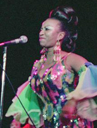 A woman in colorful dress on stage with microphone.