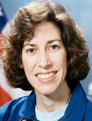 A woman with brown hair and blue shirt smiling.