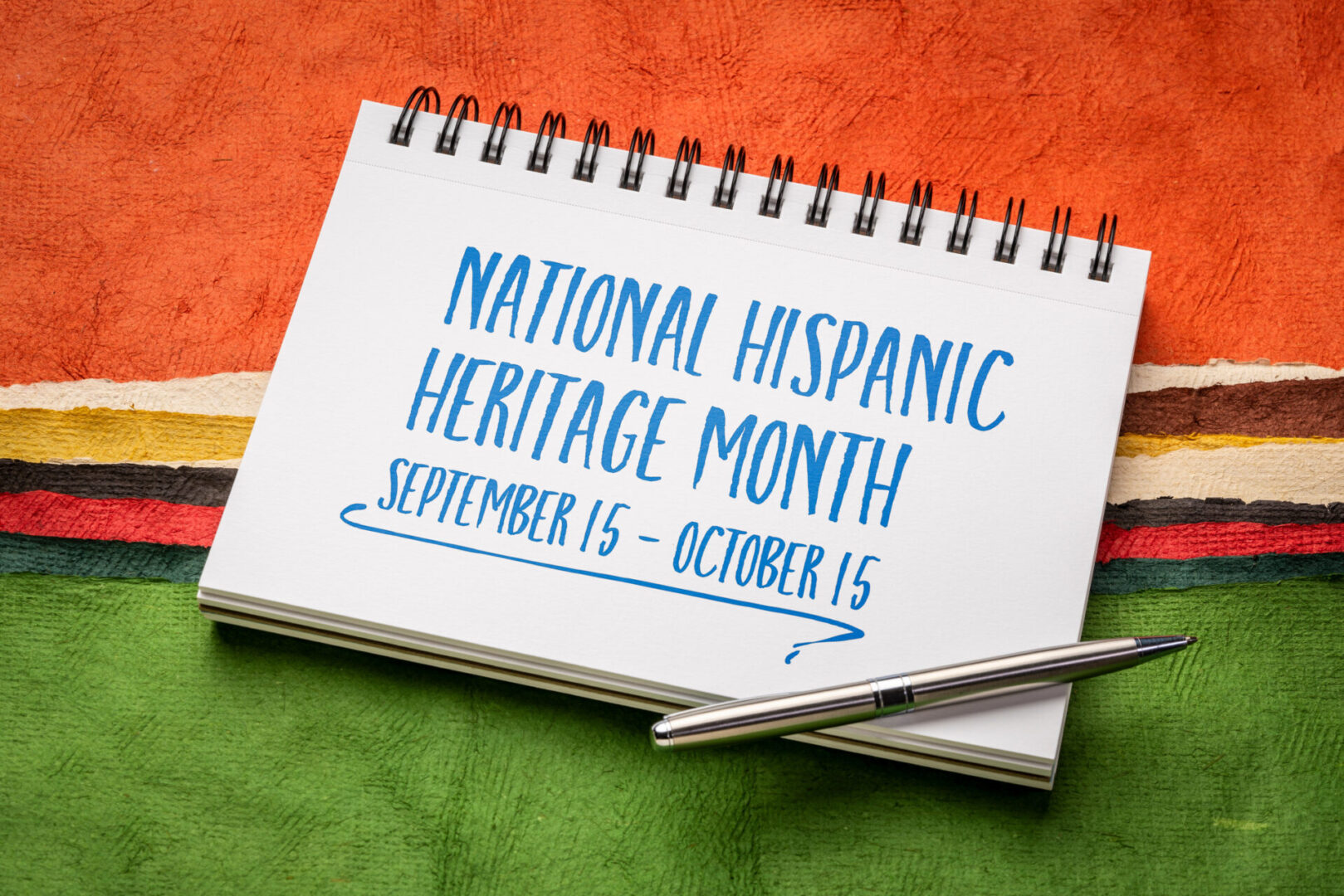 September 15 - October 15, National Hispanic Heritage Month - handwriting in in a spiral notebook against abstract landscape created with Mexican Huun paper, reminder of cultural event